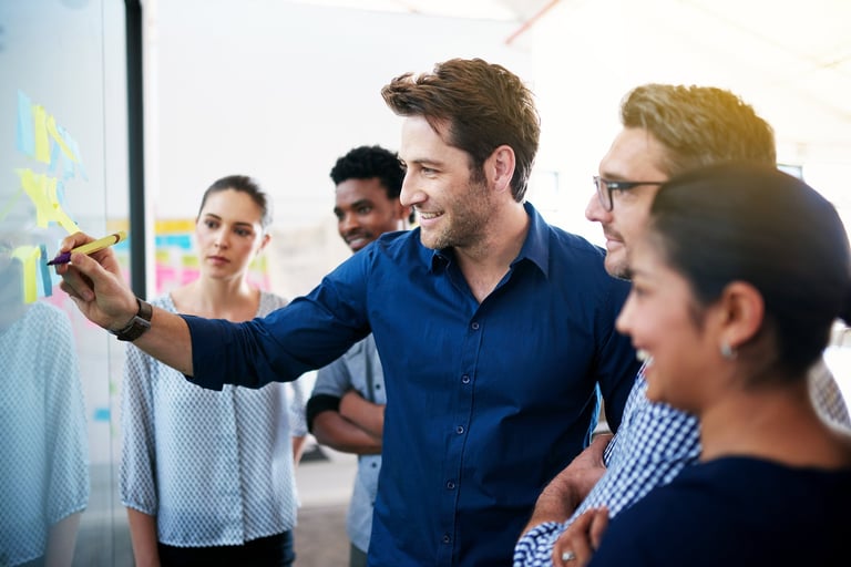 Group of colleagues brainstorming together on a glass wall with sticky notes, representing strategic planning and clear direction